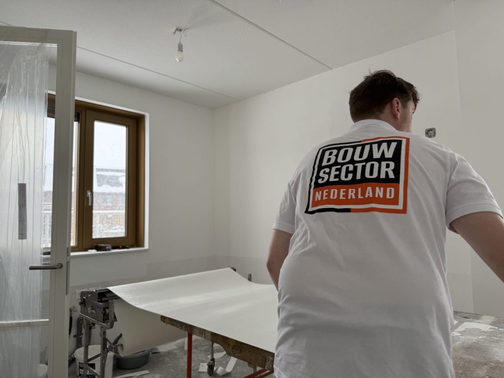 Behanger van Bouwsector Nederland bij de plaktafel met een baan vlies in een lege kamer