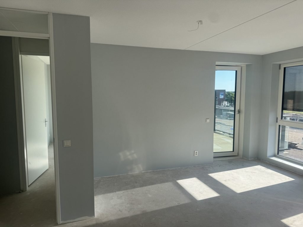 Lege nieuwbouwkamer met egaal grijze wanden en een doorkijk naar de gang