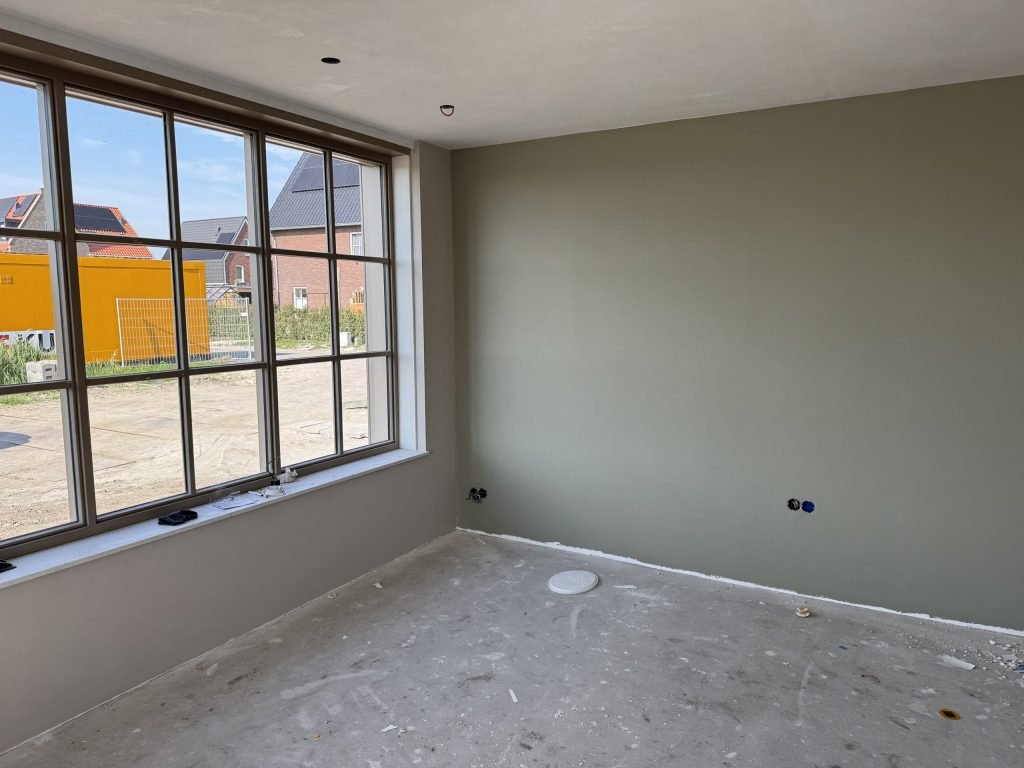 Nieuwbouwkamer met één afgewerkte wand in een grijsgroene tint naast een groot raam